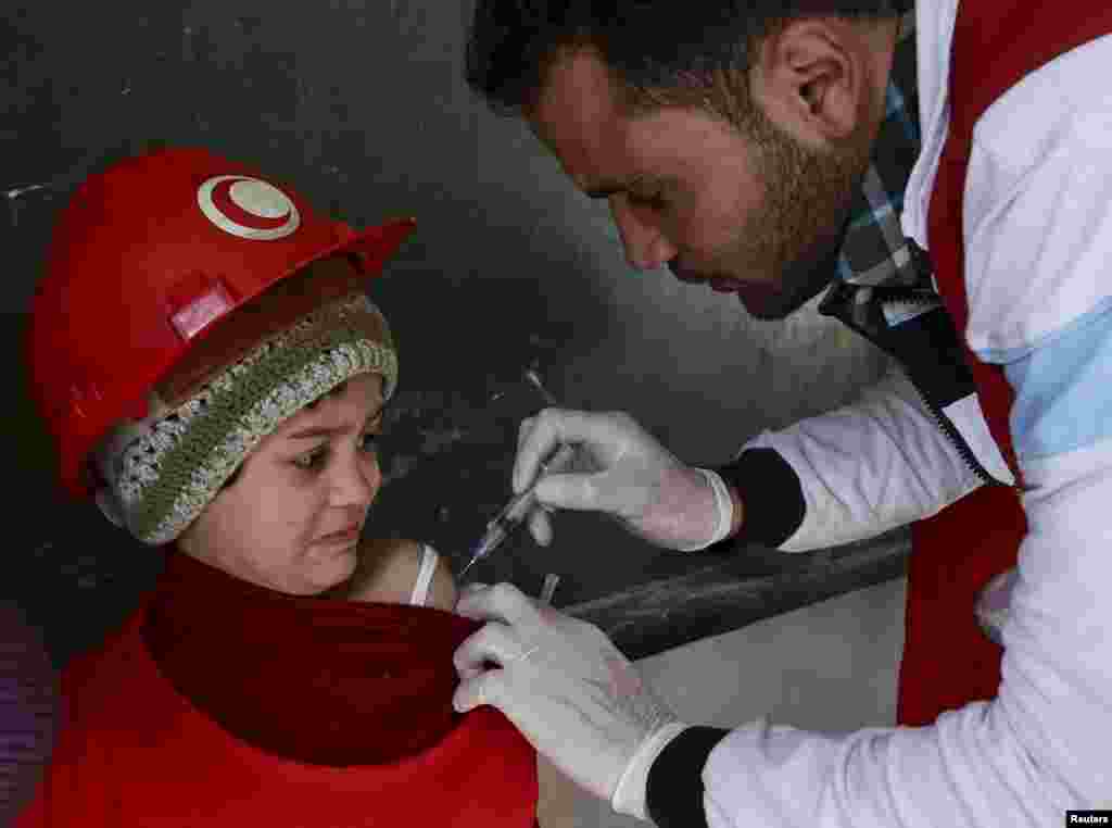 A member of the Syrian Arab Red Crescent administers a vaccination to a girl at a school in the rebel held Douma neighborhood of Damascus.