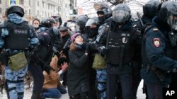 Seorang polisi menahan seorang pria, sedang rekannya menyetop seorang perempuan (tengah), saat demo menentang penahanan pemimpin oposisi Rusia, Alexei Navalny, di Moscow, Rusia, 23 Januari 2021.