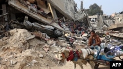 A Palestinian man rides a horse-pulled cart, next to a destroyed building where personal belongings of people and a car are sandwiched between the layers of its rubble, in Gaza City on Nov. 2, 2024.