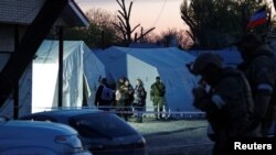 Sejumlah perempuan yang dievakuasi dari pabrik baja Azovstal di Mariupol berdiri dekat tentara pro Rusia di tempat penampungan sementara di Desa Bezimenne di tengah konflik Ukraina-Rusia di Wilayah Donetsk, Ukraina, Jumat, 6 Mei 2022. (Foto: Alexander Ermochenko/Reuters)