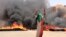 A protester wearing a Sudanese flag flashes the victory sign in front of burning tires and debris on Road 60, near Khartoum's army headquarters, in Khartoum, Sudan, June 3, 2019.