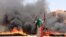 FILE - A protester wearing a Sudanese flag flashes the victory sign in front of burning tires and debris on road 60, near Khartoum's army headquarters, in Khartoum, Sudan, June 3, 2019.