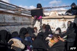FILE - Women and children fleeing from the last Islamic State group's tiny pocket in Syria sit in the back of a truck near Baghuz, eastern Syria, Feb. 11, 2019.