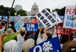 FILE - In this Aug. 30, 2015 file photo, protesters hold anti-war placards in front of the National Diet building during a rally in Tokyo.
