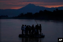 FILE - Central American migrants stand on a raft to cross the Suchiate River from Guatemala to Mexico, as the Tacana volcano stands tall near Ciudad Hidalgo, Mexico, early Monday, June 10, 2019.