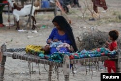 A woman, who became displaced, looks after her baby while taking refuge in a camp, following rains and floods during the monsoon season in Sehwan, Pakistan September 15, 2022. (REUTERS/Akhtar Soomro)