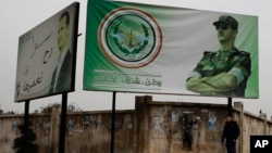 FILE - A man walks by posters of Syrian President Bashar al-Assad that in Arabic read "Homeland, honor, fidelity. Together we will build it," in Aleppo, Syria, Dec. 5, 2016.
