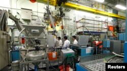 FILE - Workers look through a thick glass window as part of the treatment of nuclear waste at the Areva Nuclear Plant of La Hague, near Cherbourg, France, April 22, 2015.