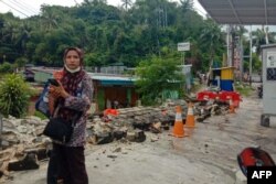 Seorang perempuan menggunakan ponselnya di samping dinding yang runtuh setelah gempa berkekuatan 5,1 di Jayapura, pada 9 Februari 2023. (Foto: AFP/FAISAL NARWAWAN)