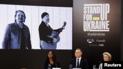 The Edge dan Bono – gitaris (kiri) dan vokalis (kanan) band U2– tampak di layar ketika Presiden Komisi Eropa Ursula von der Leyen dan Presiden Polandia Andrzej Duda menghadiri acara “Stand Up for Ukraine di Warsawa, Polandia, Sabtu, 9 April 2022. (Foto: Kacper Pempel/Reuters)