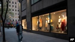 A man wearing a mask walks by a window display at a J Crew store in Rockefeller Center, May 2, 2020, in New York.
