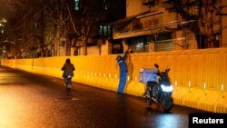 FILE - A delivery worker hands a bag to a resident behind barriers sealing off an area, before the second stage of a two-stage lockdown to curb the spread of COVID-19 in Shanghai, China, March 31, 2022. 