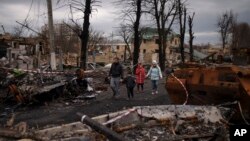 FILE - A family walks amid destroyed Russian tanks in Bucha, on the outskirts of Kyiv, Ukraine, April 6, 2022.
