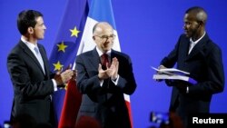French Prime Minister Manuel Valls and Interior Minister Bernard Cazeneuve applaud Lassana Bathily, 24, during his citizenship ceremony at the Interior Ministry in Paris, Jan. 20, 2015.