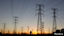 FILE - A man walks past electricity pylons as he returns from work in Soweto, outside Johannesburg.