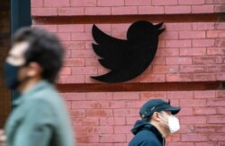FILE - People wearing face masks during the coronavirus pandemic walk by the Twitter logo outside the New York City headquarters in Manhattan, Oct. 14, 2020.