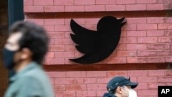 FILE - People walk by the Twitter logo outside the New York City headquarters in Manhattan, Oct. 14, 2020.