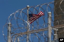 FILE - In this April 17, 2019 file photo reviewed by U.S. military officials, a U.S. flag flies inside the razor wire of the Camp VI detention facility in Guantanamo Bay Naval Base, Cuba.