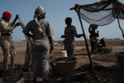Fatou Samba, right, carries on her head a basket filled with the remains of processed fish at Bargny beach, Senegal, Apr. 25, 2021.