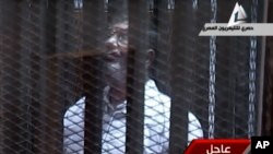 In this image taken from Egypt State TV, Mohammed Morsi stands inside a glass-encased metal cage in a courtroom in Cairo, Jan. 28. 2014. 