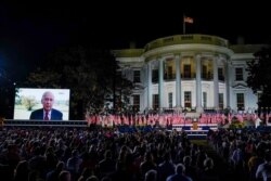 People watch video screens before President Donald Trump speaks from the South Lawn of the White House on the fourth day of the Republican National Convention, Aug. 27, 2020, in Washington.