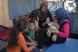 Umm Joumaa, a Syrian displaced from Hama, sits with her family in an abandoned bus in the village of Birat Armanaz in Idlib, Sept. 4, 2019.