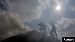 FILE - Palestinian workers rake a pile of wood as they make charcoal for sale, in the West Bank village of Yabed, June 11, 2014. 