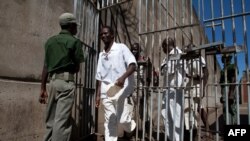 FILE - Prison Inmates walk past a prison guard at the Chikurubi Maximum security prison in Harare, Zimbabwe, May 20, 2015 during a tour by a parliamentary committee to assess the state of the nation's prisons where inmates widely complained of food shortages, over-crowding and inadequate food rations and diet. 