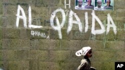 FILE - A girl walks past a wall with graffiti about the al-Qaida network in a Muslim area of the northern city of Kano, Nigeria.