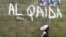 FILE - A girl walks past a wall with graffiti about the al-Qaida network in a Muslim area of the northern city of Kano, Nigeria.