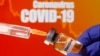 FILE PHOTO: A small bottle labeled with a "Vaccine" sticker is held near a medical syringe in front of displayed "Coronavirus COVID-19" words in this illustration taken April 10, 2020.