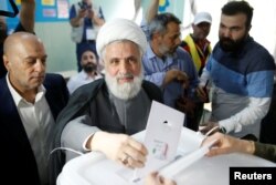 FILE - Lebanon's Hezbollah deputy leader, Sheikh Naim Qassem, casts his vote as he stands next to Hezbollah parliament candidate Amin Sherri at a polling station during the parliamentary election, in Beirut, Lebanon, May 6, 2018.