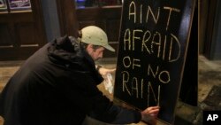 Nick Eberlein, bartender at The Merry Widow, draws a new sign as Tropical Storm Gordon arrives at night, Sept. 4, 2018, in Mobile, Ala. Tropical-force winds from fast-moving Gordon smashed into the coastline of Alabama and the western Florida Panhandle Tuesday evening.