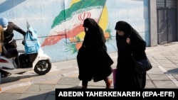 资料照片: 2022年1月22日伊朗德黑兰街道上伊朗妇女走在伊朗国旗的壁画旁。