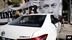 Para demonstran memegang spanduk protes mereka saat para polisi penyidik tiba di kediaman Perdana Menteri Netanyahu di Yerusalem, 17 Agustus 2018. 