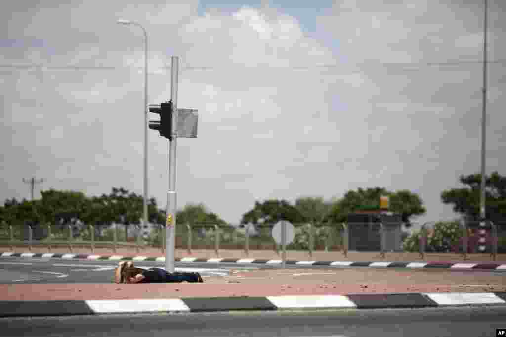 An Israeli woman takes cover as siren alarming sounds warning of rocket attacks by Palestinians militants from Gaza Strip in Ashkelon, southern Israel, July 14, 2014.