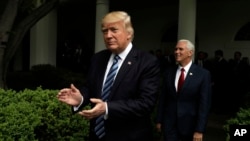 President Donald Trump claps as he arrives in the Rose Garden of the White House in Washington, followed by Vice President Mike Pence after the House pushed through a health care bill, May 4, 2017.