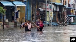 Sebuah keluarga mengarungi jalan yang tergenang banjir di Chennai, India, Rabu, 25 November 2020. Pada 19 November 2021, pihak berwenang negara bagian Andhra Pradesh, India mengatakan sedikitnya 17 orang tewas dan puluhan dilaporkan hilang setelah hujan lebat. (Foto: AP)