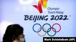 រូបឯកសារ៖ ស្ត្រី​ម្នាក់​ពាក់​ម៉ាស​ដើម្បី​ការពារ​ពី​ជំងឺ​កូវីដ១៩ ដើរ​កាត់​ស្លាកសញ្ញា​កីឡា​អូឡាំពិក​រដូវ​រងា​នៅ​ទីក្រុង​ប៉េកាំង ប្រទេស​ចិន​ឆ្នាំ២០២២ ថ្ងៃទី៩ ខែធ្នូ ឆ្នាំ២០២១។ (AP Photo/Mark Schiefelbein)