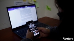 FILE - Xenia Oliva, an investigative reporter who had her phone hacked several times, including having data extracted, checks her phone at the office of GatoEncerrado in San Salvador, El Salvador, Jan. 11, 2022. 