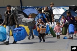 Migrants carrying their belongings walk in the Athens port of Piraeus, April 7, 2016.