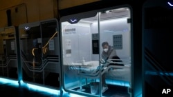 A man takes off his shoes in a sleeping pod at the main media center ahead of the 2022 Winter Olympics, Wednesday, Feb. 2, 2022, in Beijing. (AP Photo/Jae C. Hong)