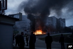 Residents stand outside their apartments as shops burn after a Russian attack in Kharkiv, Ukraine, April 11, 2022.