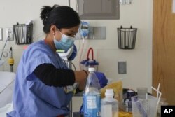 In this image provided by the U.S. Army, U.S. Air Force 1st Lt. Mary Coleman, a nurse assigned to a military medical team, prepares a patient's medication while supporting the COVID-19 response operations at University of Rochester Medical Center in Rochester, N.Y., March 5, 2022. (Spc. Khalan Moore/U.S. Army via AP)