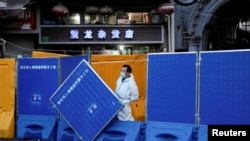 上海一名身穿防护服的工作人员站在封城使用的围栏旁。（2022年4月11日）