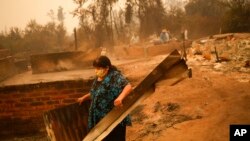 A woman clears debris from a landscape of charred remains in Santa Ana, Chile, Feb. 4, 2023.