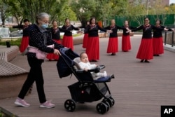 资料照：一名老年妇女推着一个婴儿走过北京一所公园里跳广场舞的妇女。（2021年10月14日）