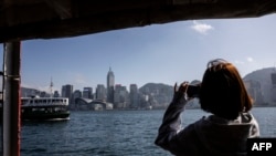 Seorang perempuan mengambil foto dari atas kapal feri di Hong Kong, 2 Februari 2023. Hong Kong menawarkan penerbangan gratis dan voucer untuk merayu wisatawan dalam upaya mengatasi persaingan regional yang sengit. (ISAAC LAWRENCE / AFP)
