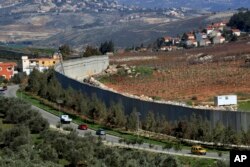 Mobil melaju di samping tembok yang memisahkan Lebanon dari Israel di desa Kfar Kila, Lebanon tenggara, Sabtu, 21 Januari 2023. Green Without Borders yang aktif di Lebanon selatan, termasuk daerah di sepanjang perbatasan dengan Israel, dituduh menjadi perpanjangan tangan Hizbullah untuk meliput beberapa kegiatan militer kelompok itu oleh Israel, AS, dan beberapa di Lebanon. (AP/Mohammed Zaatari)