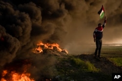 Palestinians burn tires and wave the national flag during a protest against Israeli military raid in the West Bank city of Jenin, along the border fence with Israel, in east of Gaza City Jan. 26, 2023.